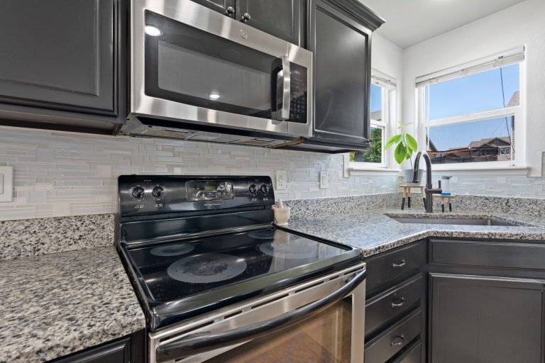 Modern kitchen with granite countertops, stainless steel appliances, and a shiny, light grey backsplash in Naples.