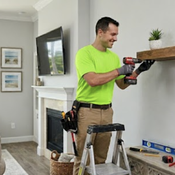 A handyman in a neon green shirt using a drill to install a shelf in a living room in Old Naples.