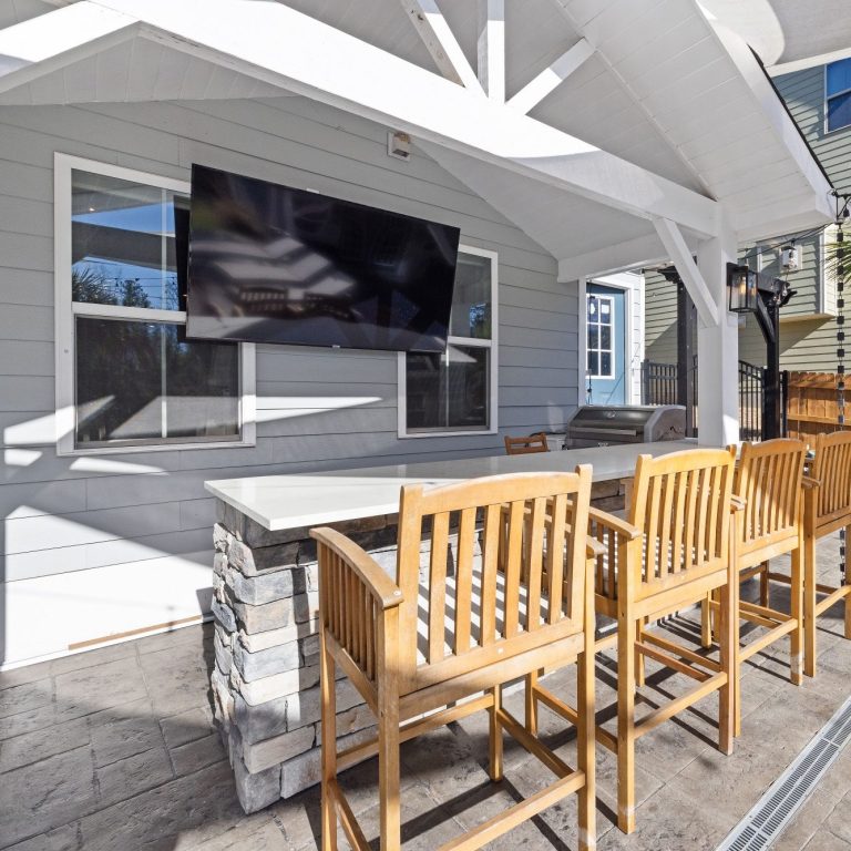 Outdoor patio with a table, bar stools, and a mounted TV on a light gray house in Naples.
