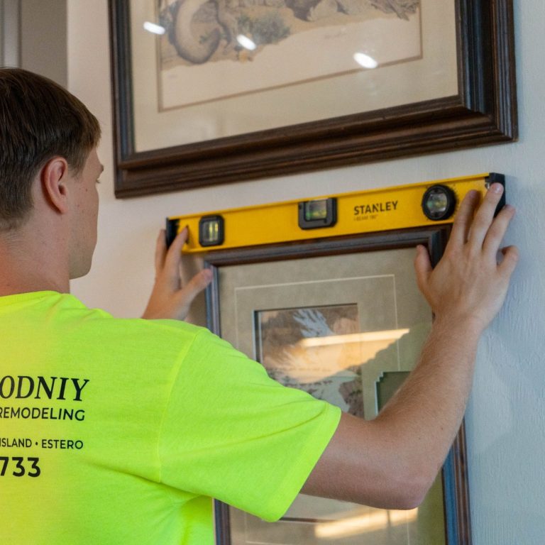A handyman using a level to make sure a photo is straight in a Naples apartment.