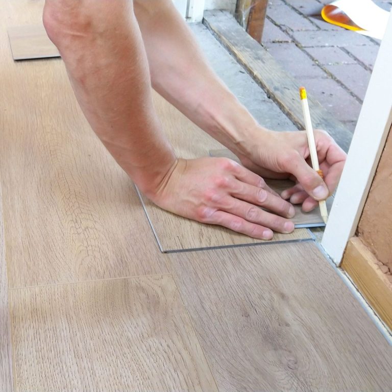 A handyman installing LVP flooring near a white door frame in Bonita Springs.