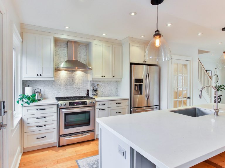 Modern kitchen with stainless steel appliances, white cabinets, and an island with a sink remodeled in North Naples.