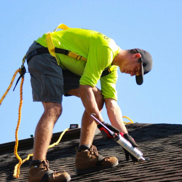 One of our handyman works on a roof, using caulking to do roof repairs.