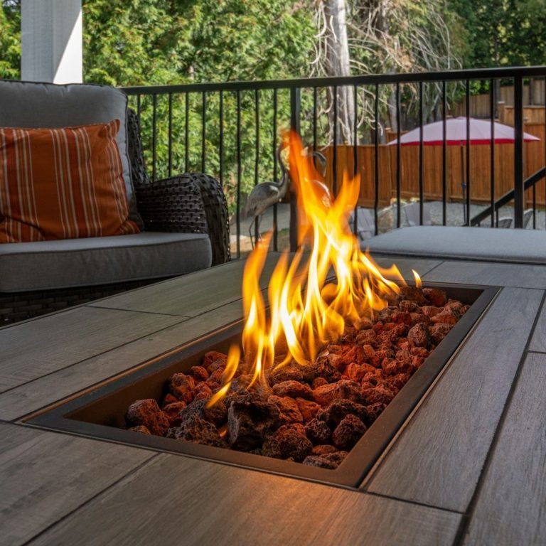 A modern outdoor fire pit with flames and decorative rocks, surrounded by chairs in Old Naples.