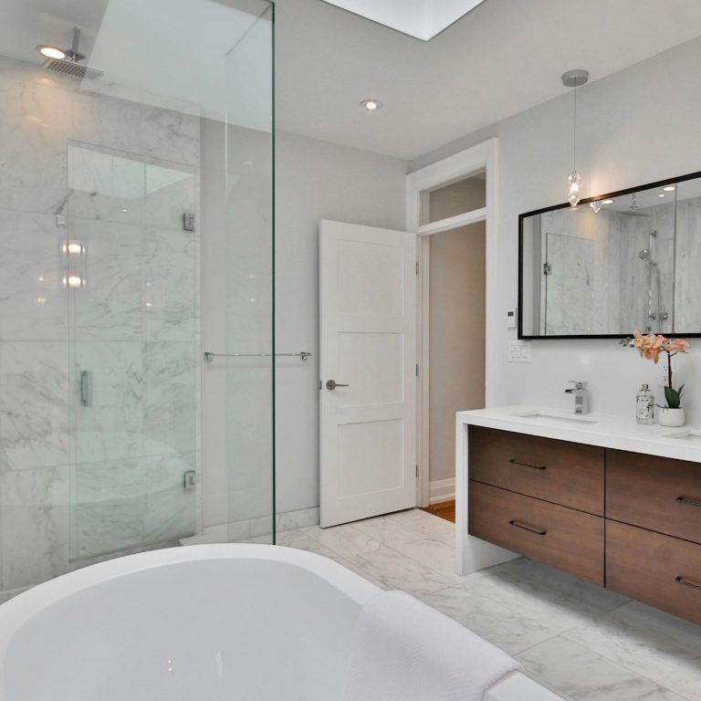 Modern bathroom with a custom tile shower, white tub, and wooden vanity under bright lighting in Marco Island.
